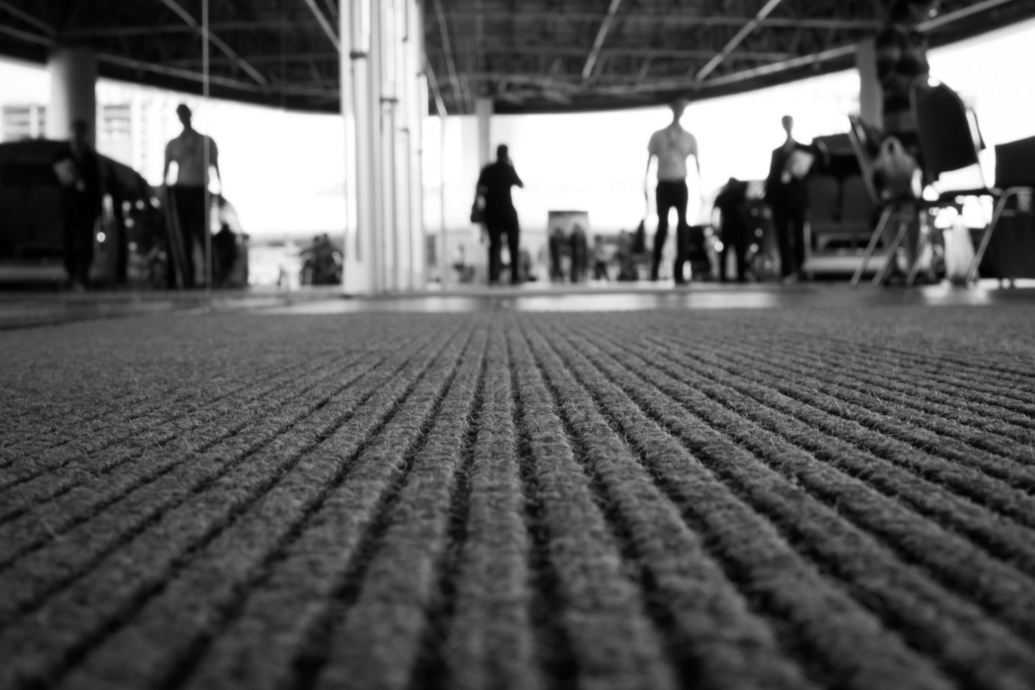 Perspective of doormat with background is blur of people. (selective focus, back and white image)